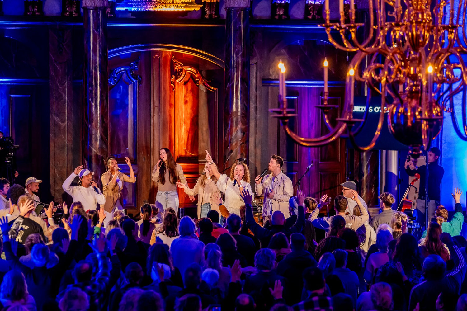 Ilaisa leading Presence Tour live worship with band in ornate venue, crowd raising hands in praise