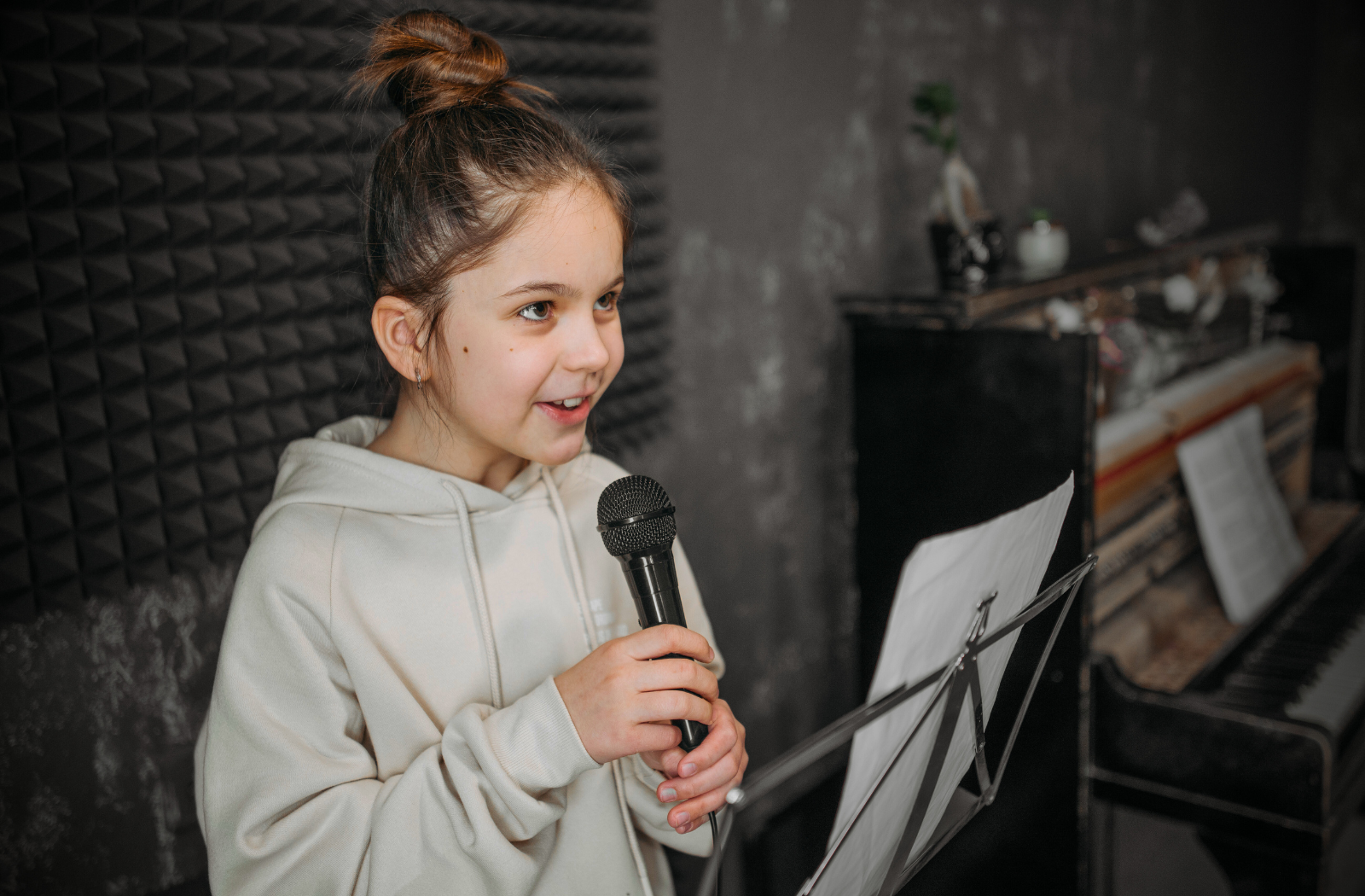 Young girl holding a microphone and reading sheet music during Ilaisa’s kids singing lesson in the studio