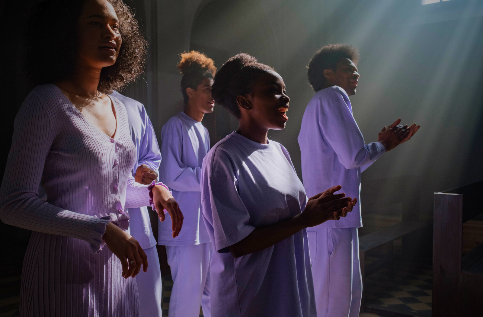 Gospel singers in lavender outfits clapping and singing under stage light during Ilaisa’s vocal workshop