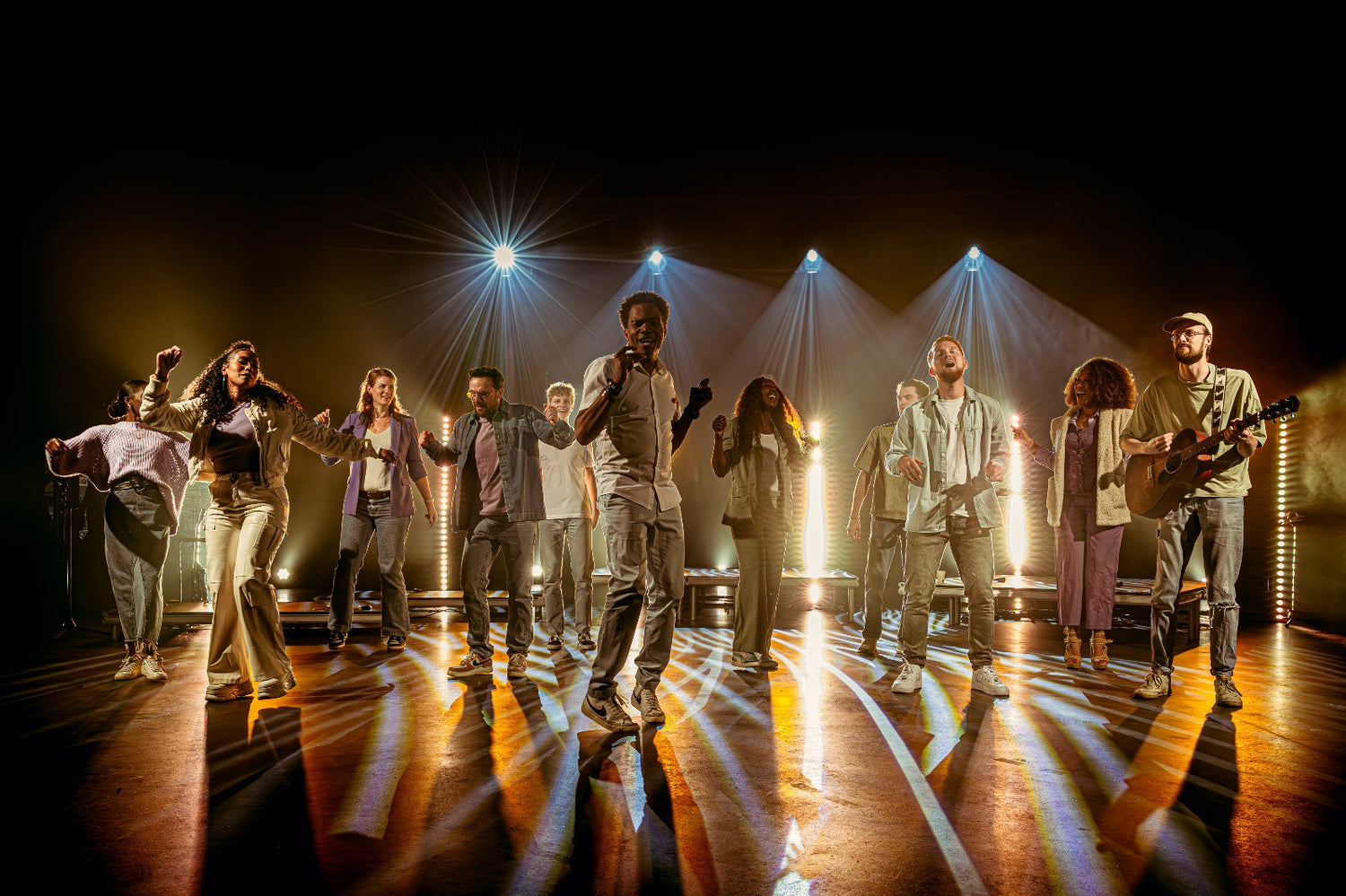 Ilaisa and ensemble performing on a spotlight-lit stage, showcasing collaborative music projects